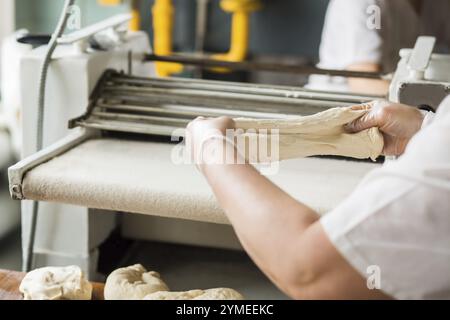 Bäckerin, die in der Bäckerei mit Teig arbeitet. Backwarenförderer im Hintergrund. Konditorei in der Lebensmittelfabrik Stockfoto