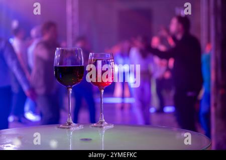 Zwei Weingläser auf einem Tisch bei einer lebhaften Party mit bunten Lichtern und Leuten, die im Hintergrund tanzen. Stockfoto