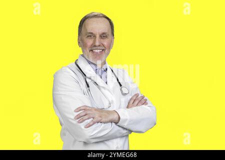 Porträt eines glücklichen Oberarztes mit gefalteten Armen. Isoliert auf Gelb Stockfoto
