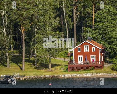 Bezauberndes rotes Haus am Rande des Waldes mit einem Boot auf dem Wasser in der Nähe, Archipel, stockholm, schweden Stockfoto