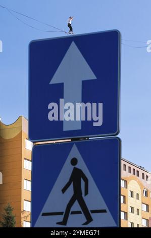 Ein Straßenschild, über dem Sie eine Person sehen können, die in der Ferne auf einem Seilseil läuft Stockfoto