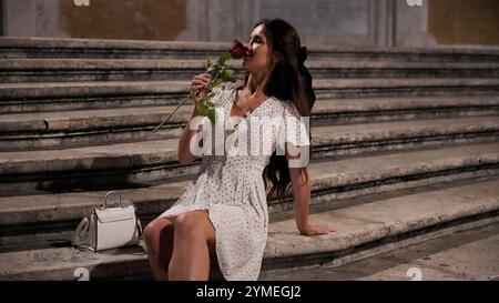 Romantischer Abend. Frau mit Rose, die auf der historischen Treppe in Rom sitzt Stockfoto