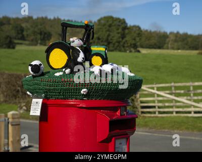 Nahaufnahme der Garn Bomb auf rotem Briefkasten (Ausstellung der Farm-Szene, dekorative Garn-Bombenbombe Street Art) - Bolton Abbey Village, North Yorkshire, England Großbritannien. Stockfoto