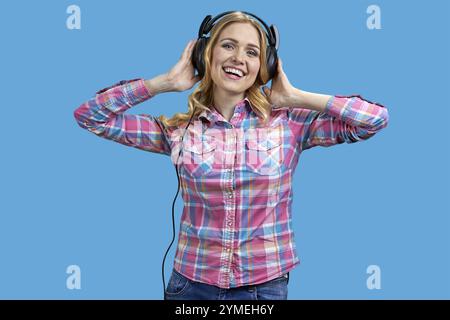 Glückliches, fröhliches Mädchen, das Musik hört und in die Kamera schaut. Attraktive junge Frau, die Spaß hat, während sie Musik auf farbigem Hintergrund hört Stockfoto