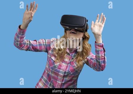 Aufgeregtes Mädchen mit Virtual-Reality-Headset auf blauem Hintergrund. Die Frau benutzt eine virtuelle Brille Stockfoto