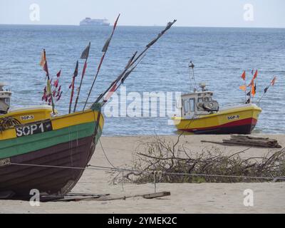 Farbenfrohe Boote am Strand mit Flaggen und einem fernen Schiff am Horizont, sopot, ostsee, polen Stockfoto