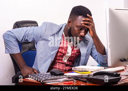 Junger besorgter Geschäftsmann, der mit Blick auf den Laptop im Büro sitzt und Hand auf Kopf hält. Stockfoto