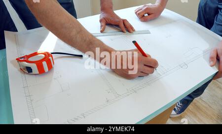 Zwei Arbeiter entwickeln einen Plan für das Haus. Das Projekt ist auf Papier gezeichnet Stockfoto