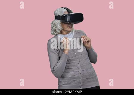 Verängstigte Seniorin mit virtueller Brille auf farbigem Hintergrund. Mensch und modernes Technologiekonzept Stockfoto