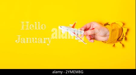 Hand hält ein Spielzeug Flugzeug vor einem gelben Hintergrund mit den Worten Hello January unten Stockfoto