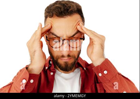 Nahaufnahme eines kaukasischen Mannes, der mit beiden Händen seine Schläfe drückt, tief in Gedanken oder gestresst erscheint, mit Brille und einem roten Hemd, stehend auf isoliertem weißem Hintergrund Stockfoto