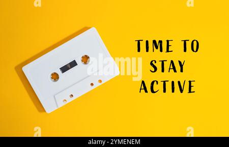 Das weiße Kassettenband ist auf gelbem Hintergrund mit der Aufschrift „Time to Stay Active“ (Zeit zum Verbleib aktiv) darunter Stockfoto