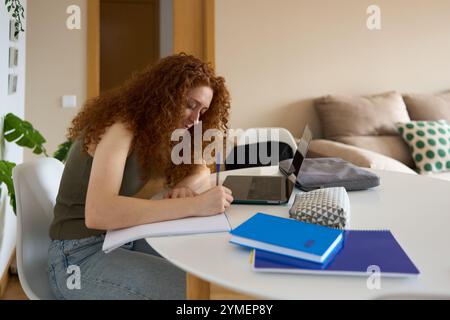 Junge Schüler, die Notizen schreiben, während sie zu Hause mit einem Laptop studieren Stockfoto