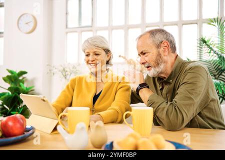 Seniorenpaar mit digitalem Tablet zu Hause beim Frühstück Stockfoto