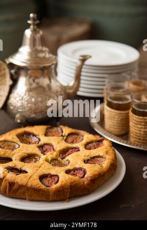 Traditioneller marokkanischer Tee mit Feigenkuchen, serviert auf einem rustikalen Holztisch mit kunstvollen Details, kultureller Authentizität und süßem Genuss. Stockfoto