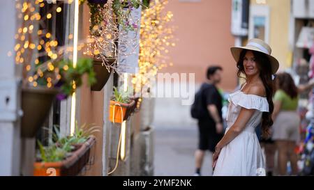 Elegante Frau, die eine malerische Gasse in Rom erkundet, die mit Feenlicht geschmückt ist Stockfoto
