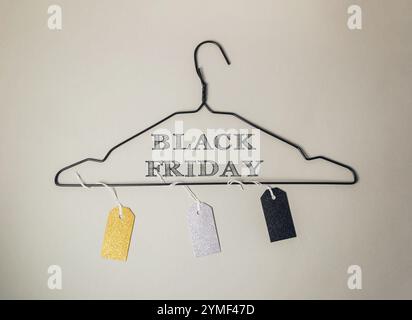 Schwarz-weißes Schild hängt an einem Kleiderbügel, auf dem steht "Black Friday". Das Schild ist mit Anhängern verziert und hat ein goldenes und silbernes Farbschema Stockfoto