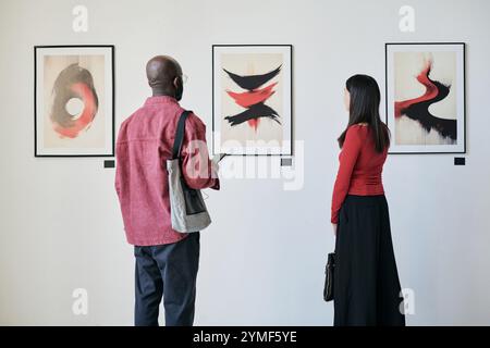 Besucher bewundern abstrakte Kunstwerke in modernen Galerieausstellungen. Mann und Frau fokussierten sich auf Gemälde und beschäftigten sich intensiv mit ausgestellten Kunstwerken Stockfoto