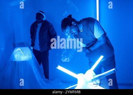 Zwei Personen, die in einem blau beleuchteten Raum mit fortschrittlicher Technologie interagieren, schaffen ein immersives und futuristisches Ambiente. Die Highlights von Neonlichtern verbessern die Sci-fi-Atmosphäre Stockfoto