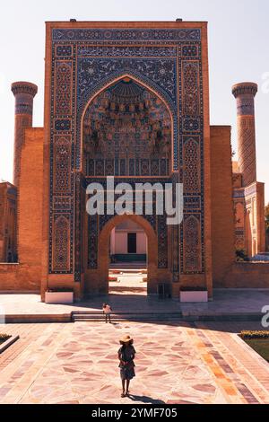 Zwei Kinder werden bei einem Spaziergang aus dem großen Amir Temur Mausoleum in Usbekistan an einem hellen sonnigen Tag gefangen. Der prächtige bogenförmige Eingang flankiert B Stockfoto