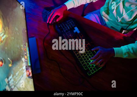Zugeschnittenes Foto des jungen Mannes verwenden Tastatur Maus sitzen Tisch Spiel Gamer Computerspiel Late Night blau lila Indoor Haus Late Neon Licht Stockfoto