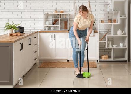 Junge Frau, die in der Küche Boden fegt Stockfoto