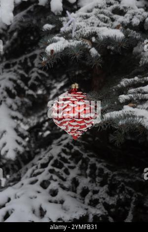 Weihnachtsschmuck hängt an Fichtenzweigen in einem botanischen Garten im Freien in Kanada. Schnee hängt an den Ornamenten und Zweigen in dieser Winterszene. Stockfoto