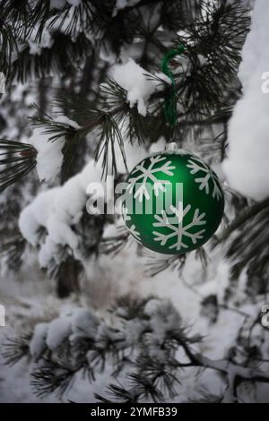 Weihnachtsschmuck hängt an Fichtenzweigen in einem botanischen Garten im Freien in Kanada. Schnee hängt an den Ornamenten und Zweigen in dieser Winterszene. Stockfoto