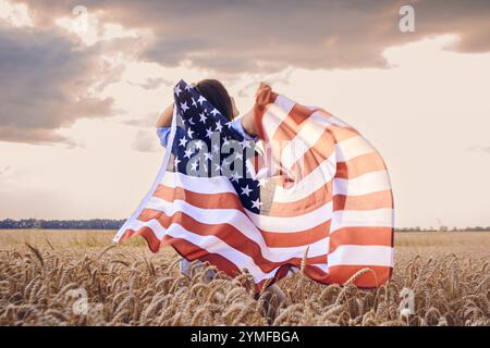 Die Frau hält eine große amerikanische Flagge auf einem Feld. Die Flagge winkt im Wind, und die Frau steht mitten auf dem Feld. Konzept der PA Stockfoto