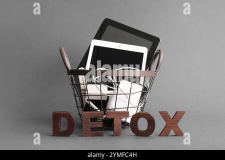 WORTENTGIFTUNG aus Holzbuchstaben und Korb mit modernen Gadgets auf grauem Hintergrund Stockfoto