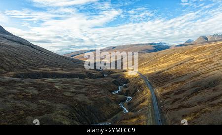 Verwinkelt gefrorener Fluss und Asphaltstraße zwischen schneebedeckten Hügeln gegen blauen Himmel. Landschaftlich reizvolle Landschaft Stockfoto