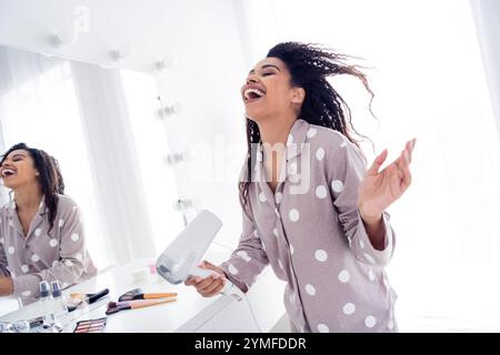 Fröhliche Morgenroutine mit einer jungen Frau im Pyjama mit Punktmuster, die zu Hause frisieren Stockfoto