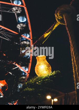 Eine brennende Glühbirne hängt an einem Baumzweig. Die Glühlampe leuchtet auf und der Baumzweig ist mit grünen Blättern bedeckt. Die Szene ist vor einem Hintergrund o Stockfoto