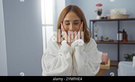 Junge Frau, die einen entspannenden Moment in einem Spa in einem weißen Bademantel mit heiterem Ausdruck genießt, in einem Wellnesscenter im Innenbereich Stockfoto