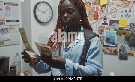 Eine junge afroamerikanische Detektivin analysiert Beweise im Untersuchungsraum einer Polizeiwache, die Geld hält. Stockfoto