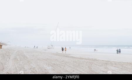 Vielfältige Gruppenwanderung am Sandy Beach mit Segelboot im Hintergrund, Wolkenkratzer Jacksonville, Florida, USA 03.15.2024 Stockfoto