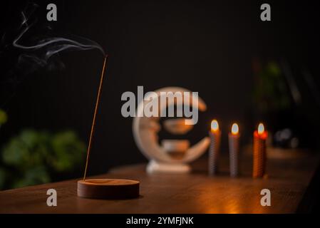 Ein Weihrauchstab brennt und erzeugt aromatischen Rauch, umgeben von kleinen Kerzen Stockfoto