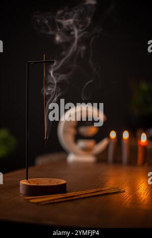Ein Weihrauchstab brennt und erzeugt aromatischen Rauch, umgeben von kleinen Kerzen Stockfoto
