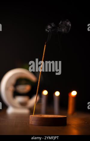 Ein Weihrauchstab brennt und erzeugt aromatischen Rauch, umgeben von kleinen Kerzen Stockfoto
