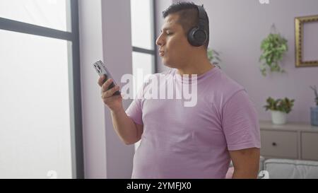 Gutaussehender hispanischer Mann, der zu Hause Musik über Kopfhörer hört und ein Smartphone hält. Stockfoto