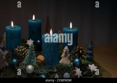 Vierter Advent, vier blau brennende Kerzen auf einem Kranz mit Weihnachtsdekoration vor dunklem Hintergrund mit Kopierraum, ausgewähltem Fokus, schmale Tiefe Stockfoto