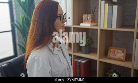 Ruhige Rothaarige Ärztin in einer Klinik, nachdenklich, mit Büchern und einer Pflanze. Stockfoto