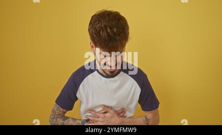 Hübscher junger hispanischer Mann mit Bart und Tätowierungen winkt vor Schmerzen gegen eine gelbe Wand Stockfoto