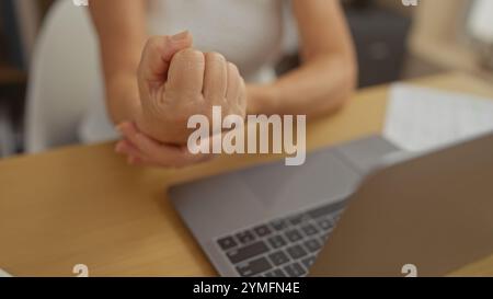 Eine kaukasierin mittleren Alters leidet zu Hause an Handgelenkschmerzen, während sie ihren Laptop benutzt. Stockfoto
