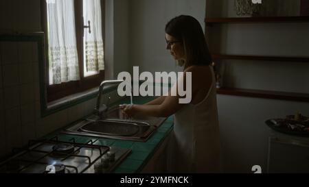 Eine junge hispanische Frau wäscht sich die Hände an einem Waschbecken in einem alten italienischen Haus mit typischer Küche. Stockfoto