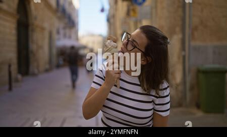 Eine junge hispanische Frau genießt es, an einem sonnigen Tag durch die bezaubernden Straßen von lecce in apulien, italien, ein Eis zu lecken. Stockfoto