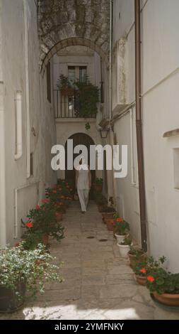 Eine wunderschöne junge hispanische Frau läuft eine enge Straße hinunter in der charmanten Altstadt von locorotondo, apulien, italien, umgeben von weißen Gebäuden und Stockfoto