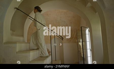 Eine wunderschöne junge hispanische Frau steigt eine Indoor-Treppe in einem typisch italienischen Haus hinauf und zeigt den architektonischen Charme einer rustikalen masseria. Stockfoto