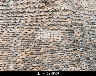 Eine Steinmauer mit einem Muster aus kleinen Steinen. Die Wand ist grau und braun. Die Steine sind so angeordnet, dass ein Gefühl von Tiefe und Tiefe entsteht Stockfoto