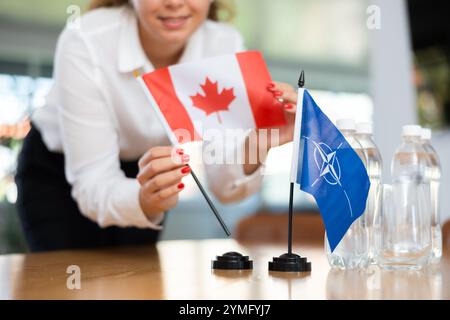 Die Sekretärin setzt die Flaggen der NATO (OTAN) und Kanadas auf den Tisch, bevor Verhandlungen mit hochrangigen politischen Persönlichkeiten geführt werden Stockfoto